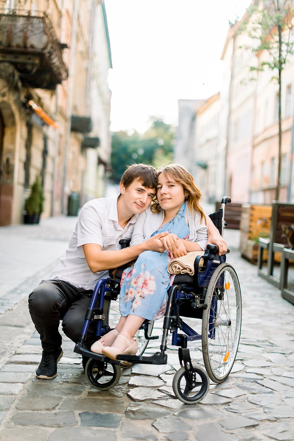A couple who is disabled embracing each other pictures on a cobblestone street.
