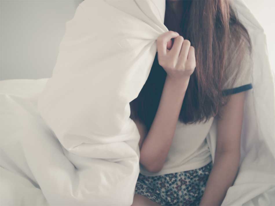 a teen with a blanket covering half of her sitting in bed.