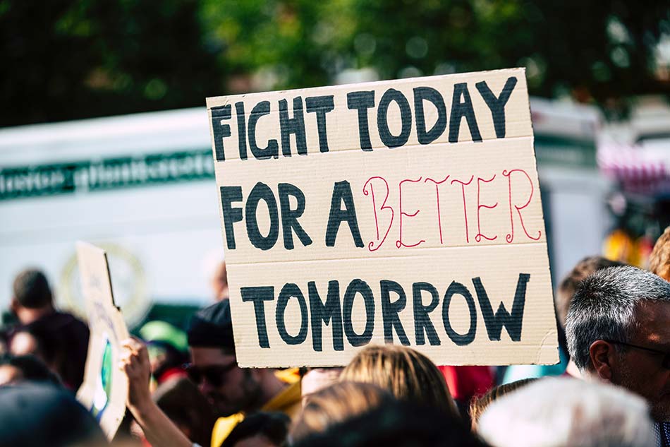 A posterboard held above a crowd that says _Fight today for a better tomorrow_