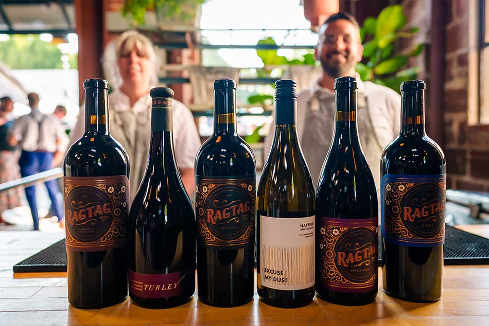 Bottles of wine on a bar with two people smiling at the camera in the background