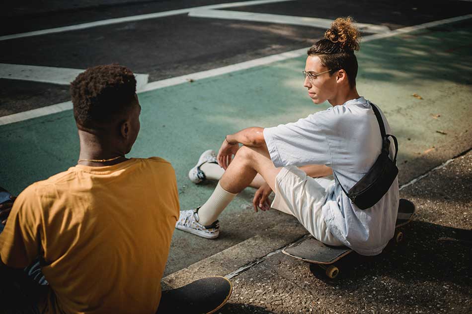 Two people talk to each other while sitting on a curb
