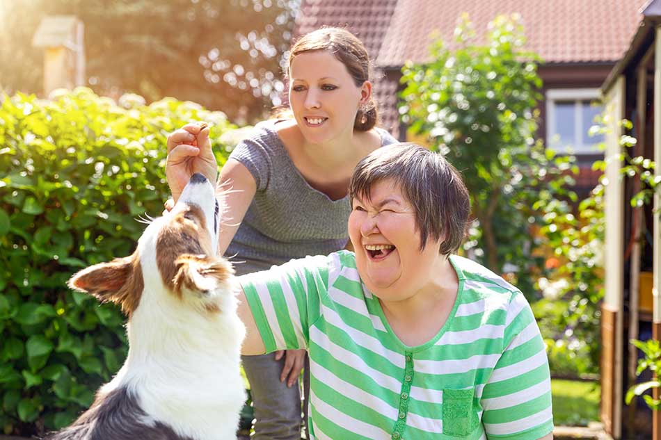 Two woman, one with a disability sat down feed a dog treats.
