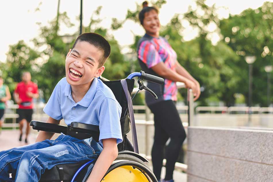 Young boy with a disability in a wheelchair laughing in a park