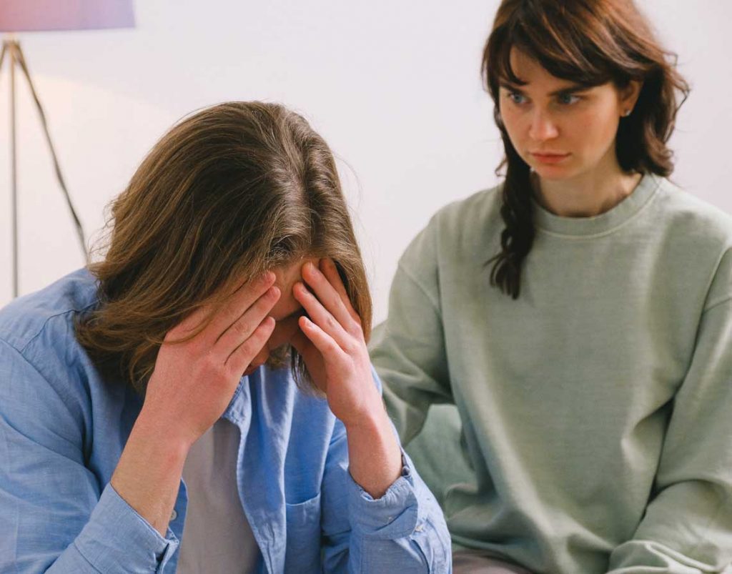 A person rests their head in their hands in frustration while a friend looks at them