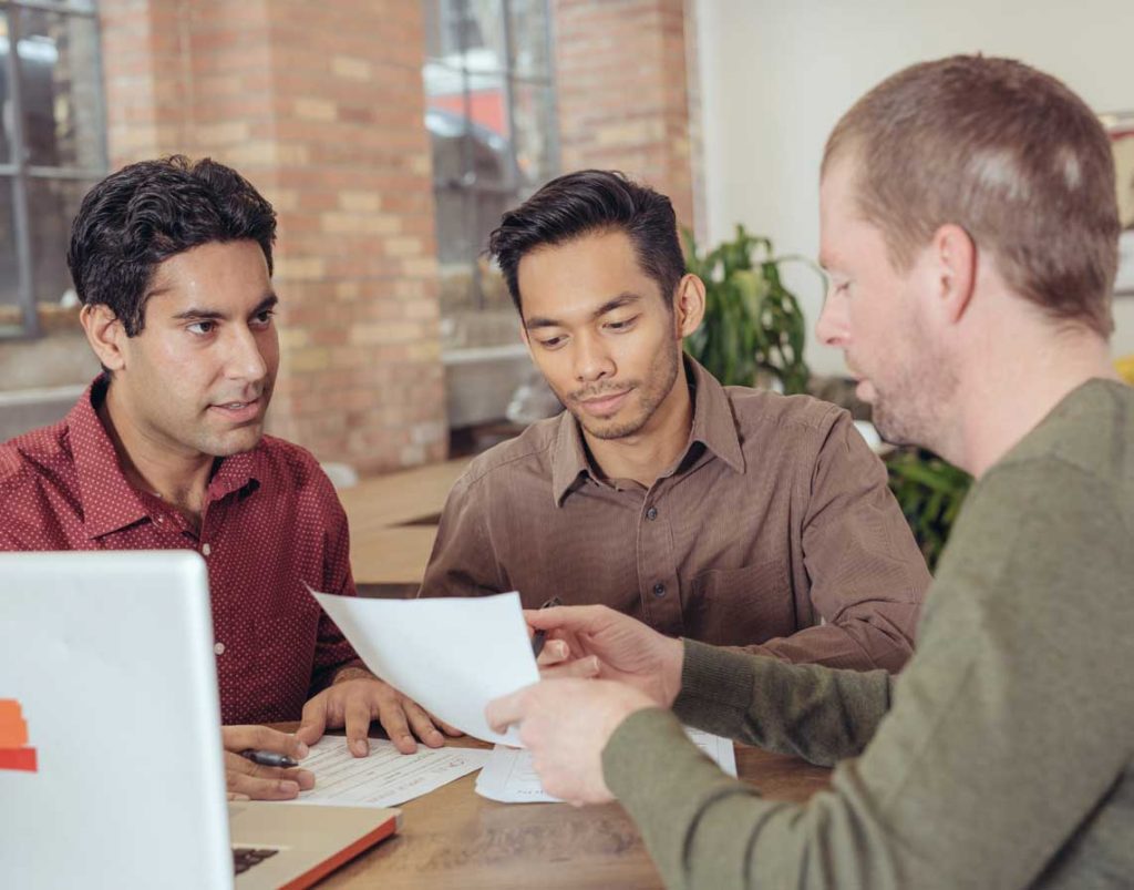 Group of three men sat at a table together discussing something.