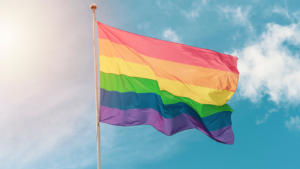 A rainbow flag in flying in a bright blue sky.