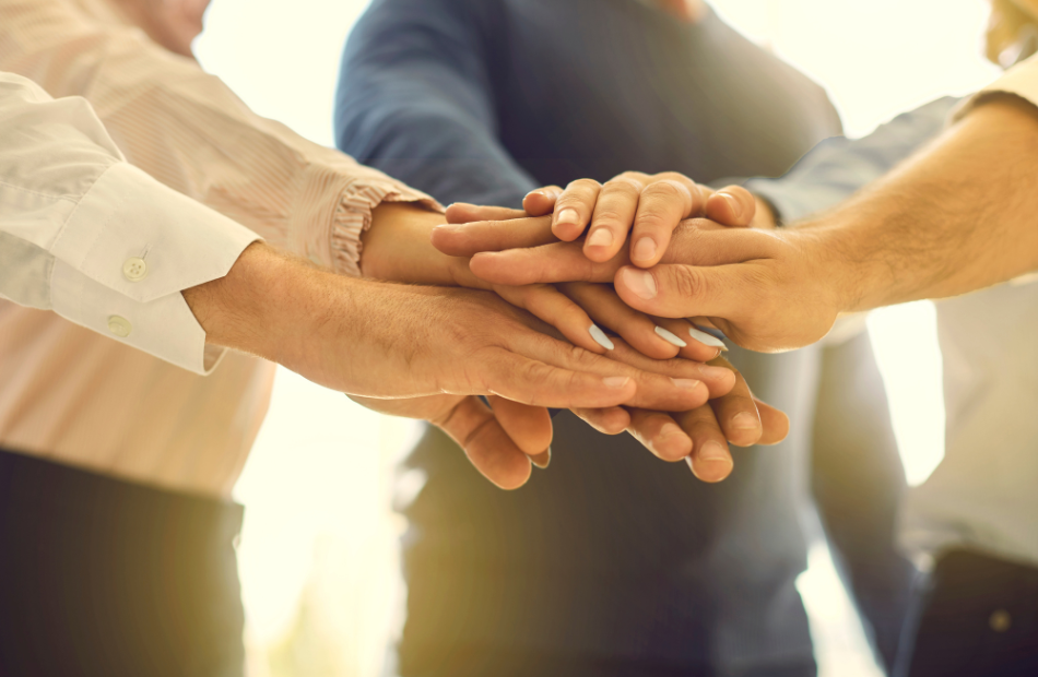 A group of people in business clothes with arms extended and their hands stacked in a circle.