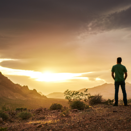 Man looking outwards towards a sunset on a mountain overlook,.