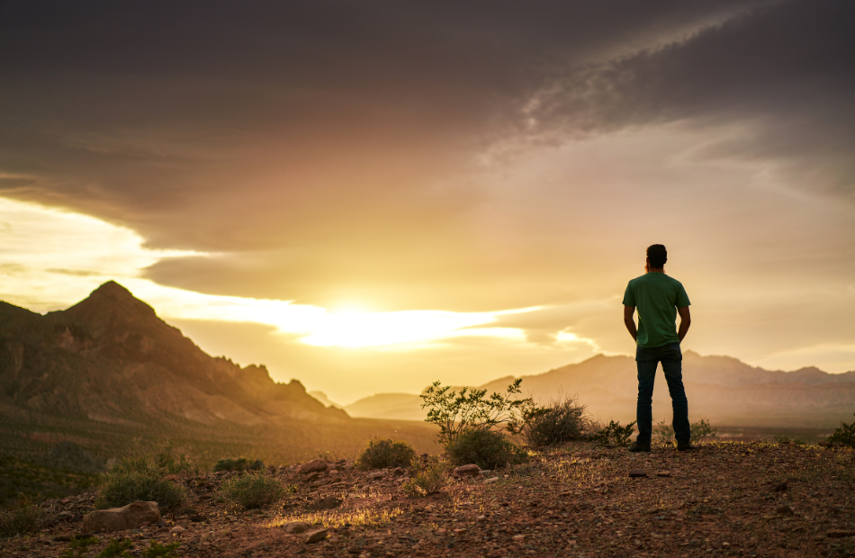 Man looking outwards towards a sunset on a mountain overlook,.