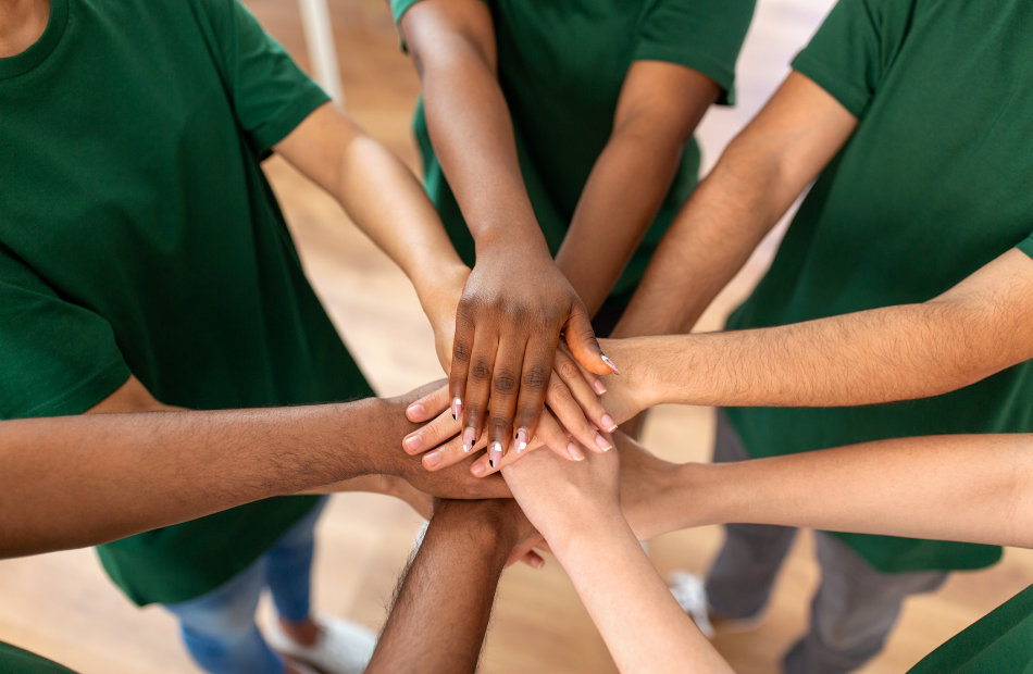 Arms extended in a circle with hands stacked. Everyone is wearing a green t-shirt.